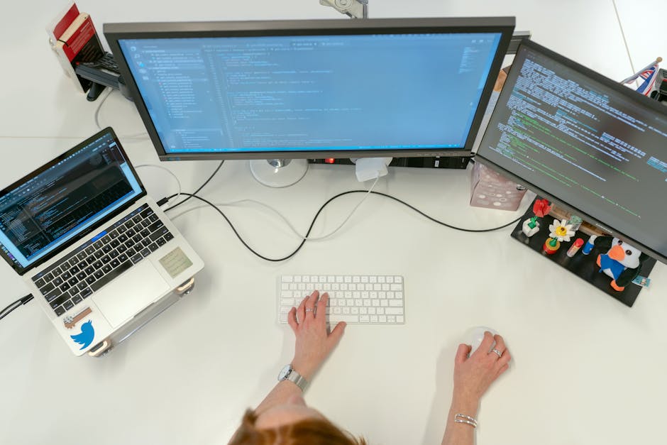 A female software engineer coding on dual monitors and a laptop in an office setting