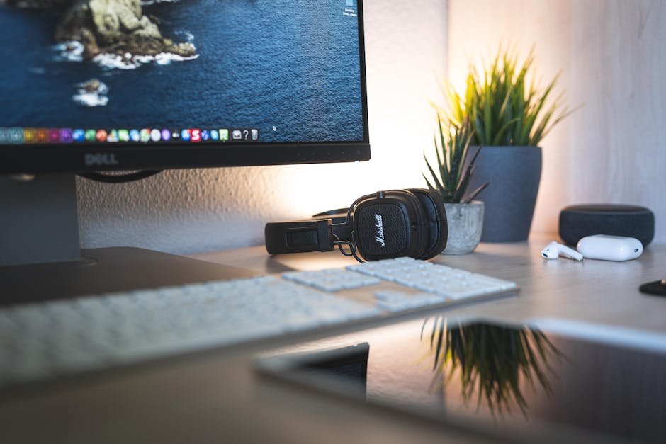 Minimalistički desk setup s monitorom, slušalicama i zelenim biljkama